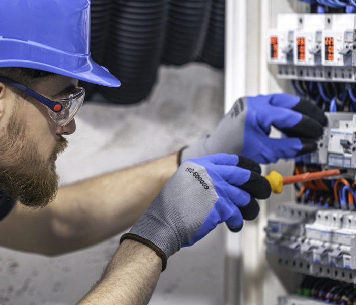 Male electrician working in a switchboard with fuses. A male electrician works in a switchboard with an electrical connecting cable.